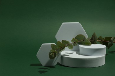Product photography props. Podiums of different geometric shapes and plant on green background, space for text