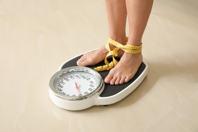 Photo of Woman with tape standing on floor scales indoors. Overweight problem