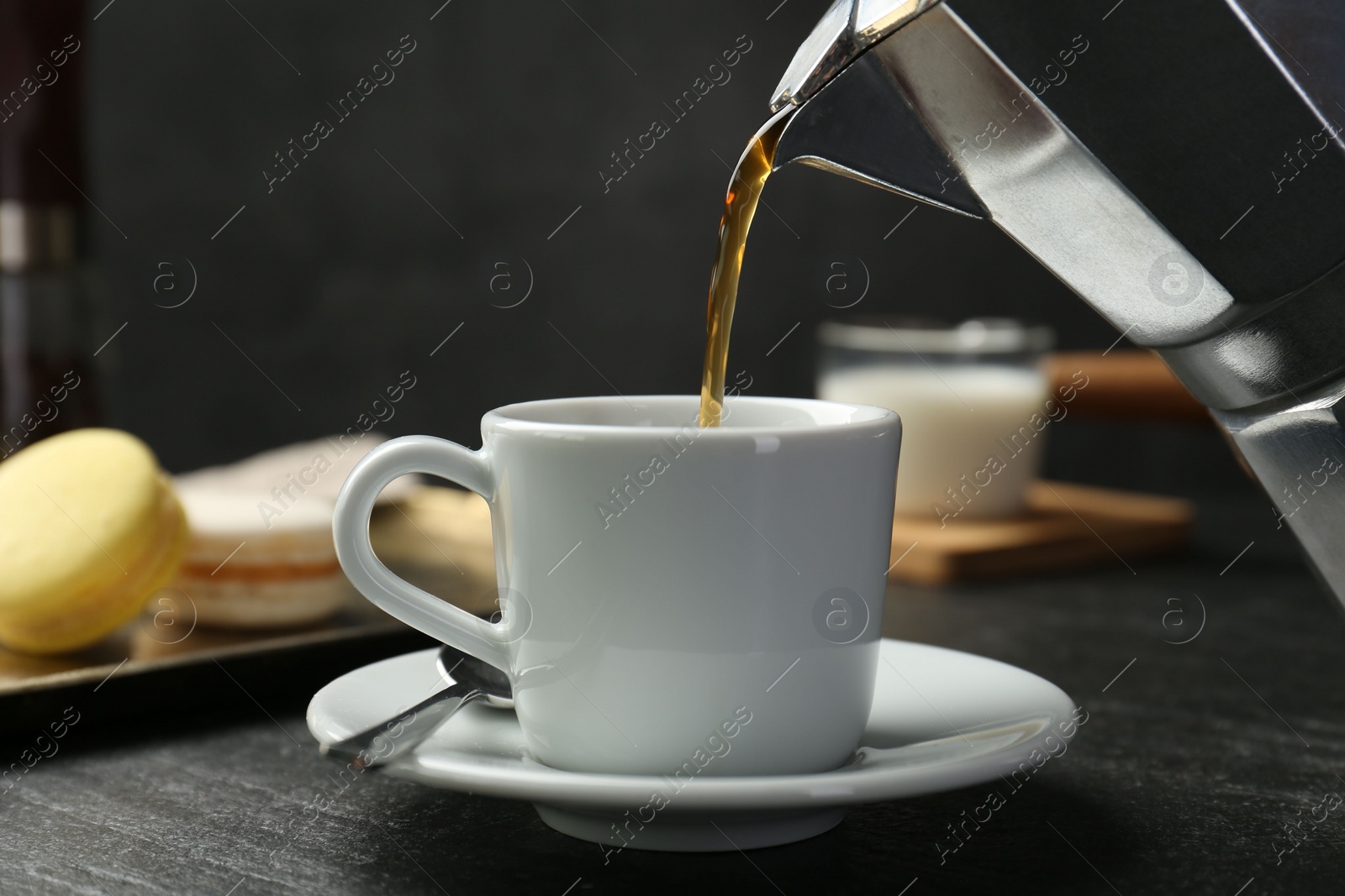 Photo of Pouring coffee from moka pot into cup at dark textured table, closeup