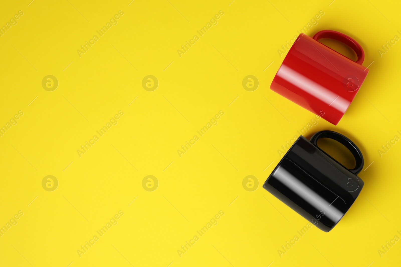 Black and red ceramic mugs on yellow background, flat lay. Space for text Photo of Black and red ceramic mugs on yellow background, flat lay. Space for text