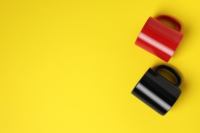 Photo of Black and red ceramic mugs on yellow background, flat lay. Space for text