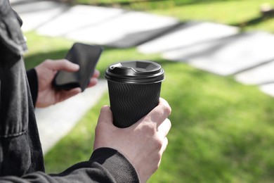 Man with smartphone holding paper coffee cup in park, closeup