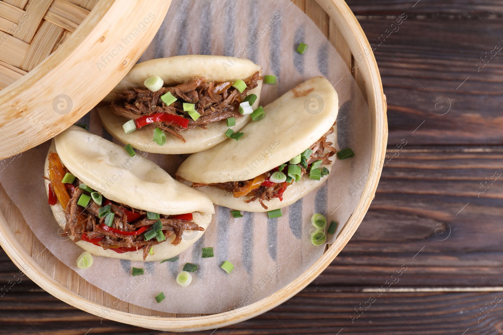 Photo of Delicious gua bao (pork belly buns) in bamboo steamer on wooden table, top view