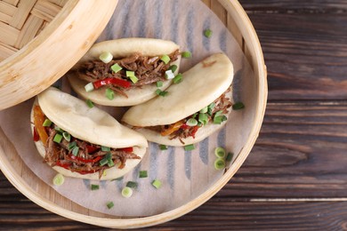 Delicious gua bao (pork belly buns) in bamboo steamer on wooden table, top view