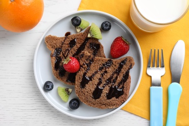 Photo of Toasts served with berries, fruits and milk on white wooden table, flat lay. Creative idea for kids breakfast