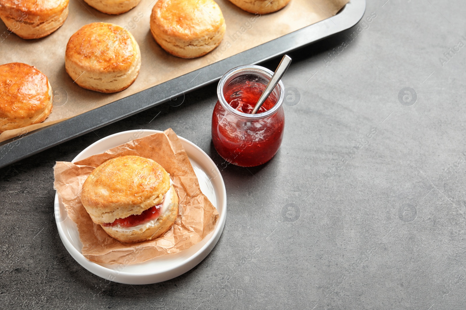 Photo of Tasty scones with clotted cream and jam on grey background