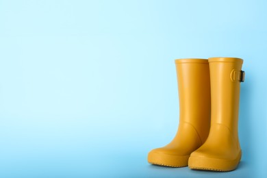 Photo of Pair of yellow rubber boots on light blue background. Space for text