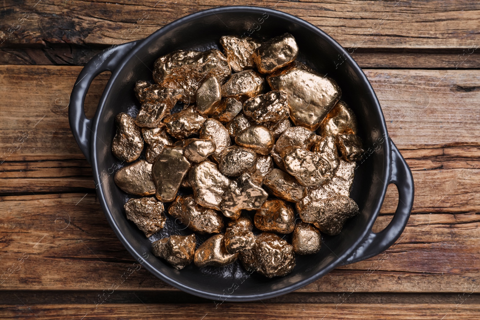 Photo of Pan of gold nuggets on wooden table, top view