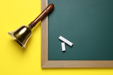 Golden bell, green board and pieces of chalk on yellow background, flat lay. School days