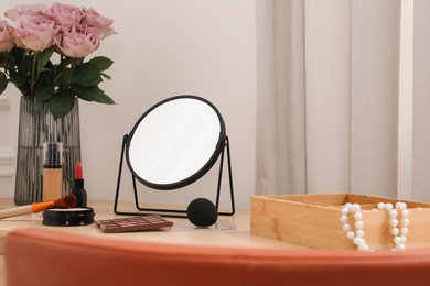 Mirror, cosmetic products, box of jewelry and vase with pink roses on wooden dressing table in makeup room