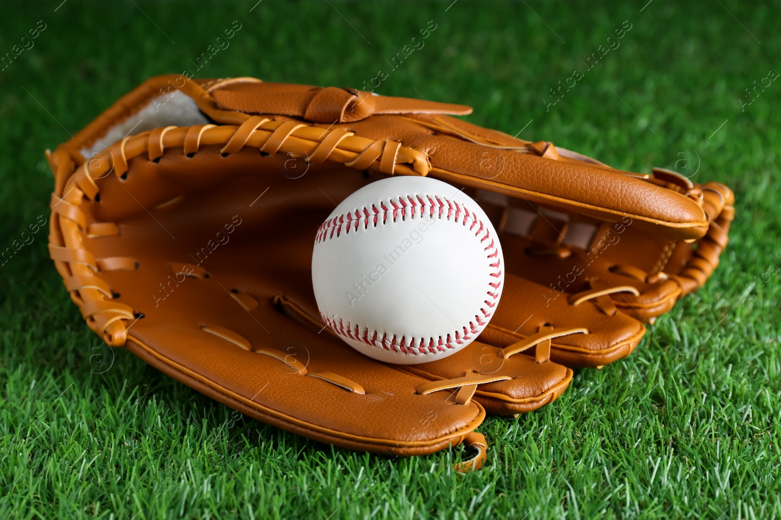 Photo of Catcher's mitt and baseball ball on green grass. Sports game