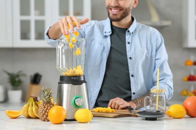 Man adding mango into blender with ingredients for smoothie in kitchen, closeup