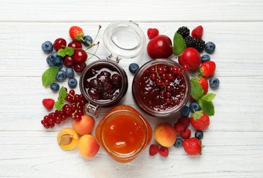 Jars with different jams and fresh fruits on white wooden table, flat lay