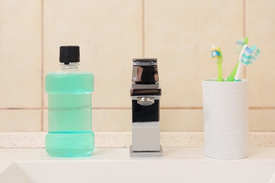 Photo of Mouthwash and holder with toothbrushes on sink in bathroom. Teeth and oral care