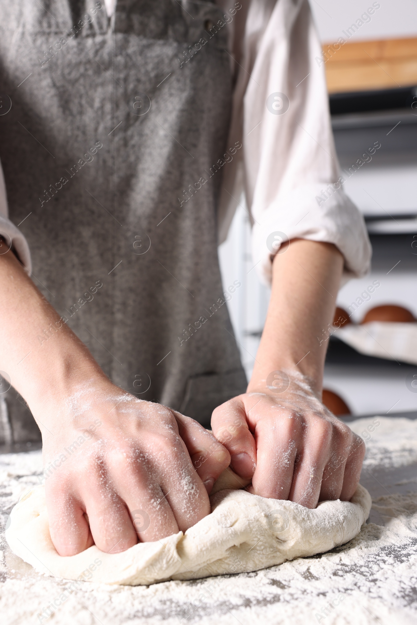 Photo of Woman kneading dough at table in kitchen, closeup