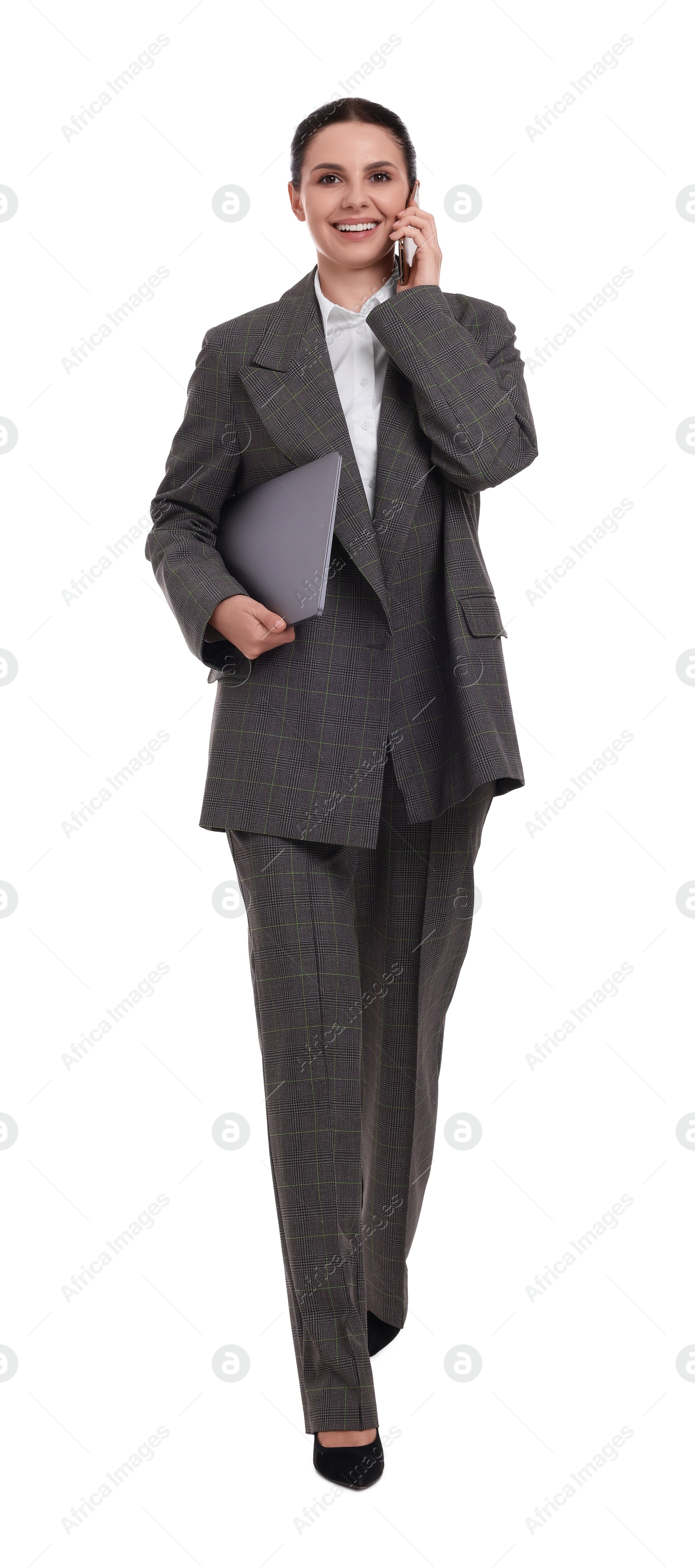 Photo of Beautiful happy businesswoman with laptop talking on smartphone while walking against white background