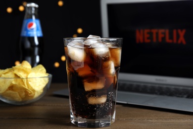 Photo of MYKOLAIV, UKRAINE - FEBRUARY 17, 2021: Pepsi with ice cubes near chips and laptop displaying Netflix on wooden table