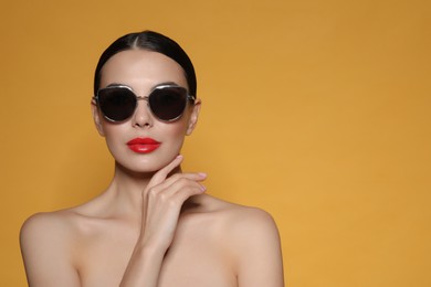 Photo of Attractive woman in fashionable sunglasses against orange background. Space for text