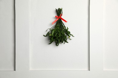 Photo of Mistletoe bunch with red bow hanging on light grey wall. Traditional Christmas decor