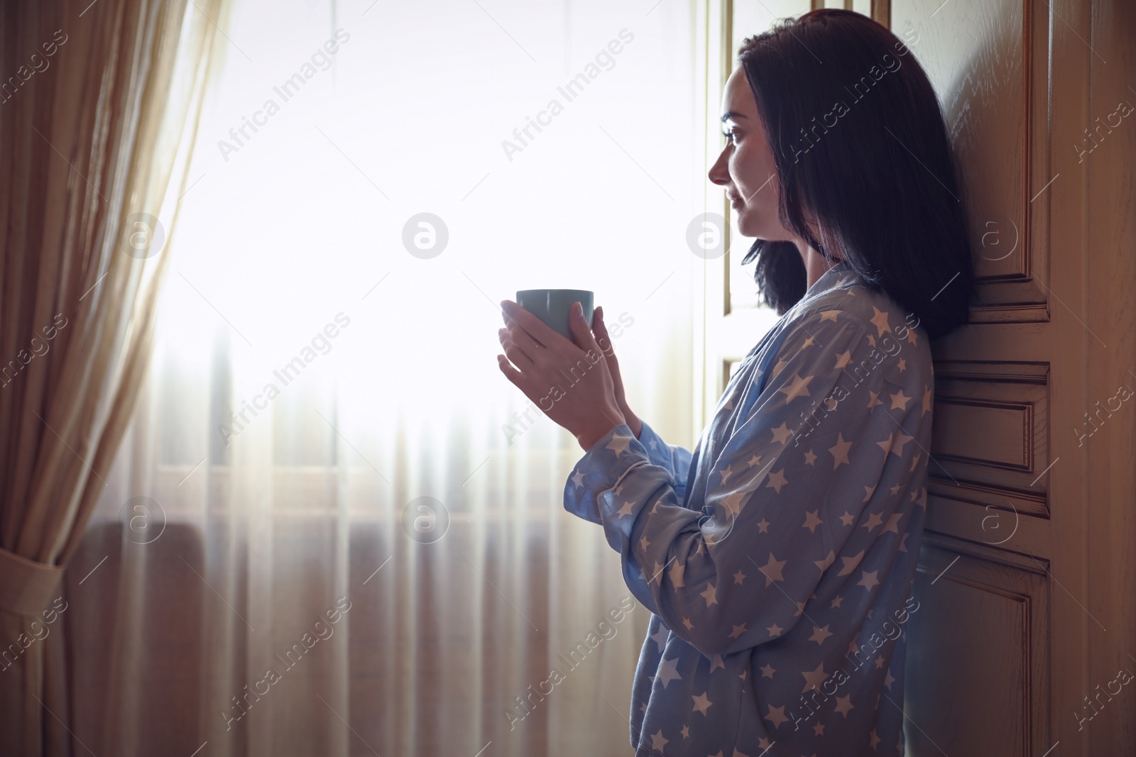 Photo of Young woman with drink near window at home. Lazy morning