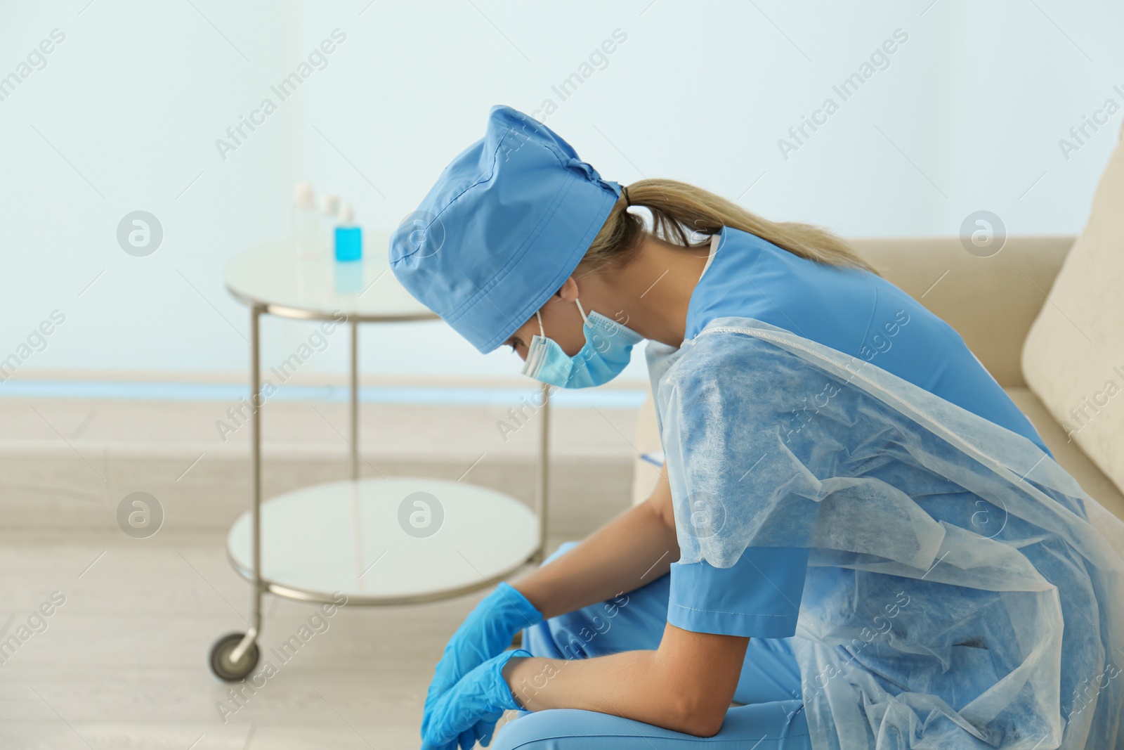 Photo of Exhausted doctor sitting on sofa indoors. Stress of health care workers during COVID-19 pandemic