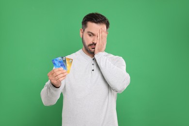 Confused man with credit cards on green background. Debt problem