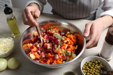 Woman preparing tasty vinaigrette salad at light wooden table, closeup