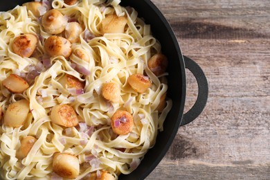 Photo of Delicious scallop pasta with onion in pan on wooden table, top view