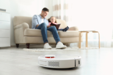 Photo of Man and his daughter resting while robotic vacuum cleaner doing its work at home