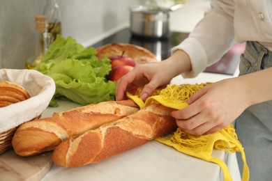 Photo of Woman taking baguettes out from string bag at countertop, closeup