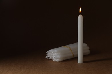 One burning and bunch of church candles on dark background, space for text