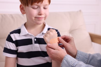 Photo of Woman putting sticking tape onto little boy`s hand on sofa, closeup
