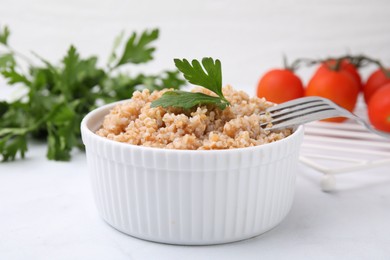 Photo of Tasty wheat porridge with parsley in bowl on white table, closeup