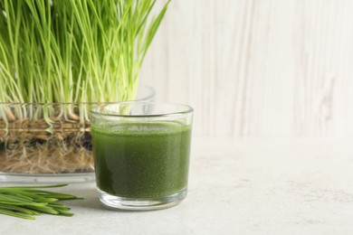 Photo of Wheat grass drink in glass and fresh sprouts on light table, space for text