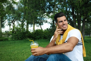 Photo of Handsome man with refreshing drink talking on smartphone in park