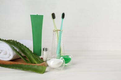 Photo of Tube of toothpaste, toothbrushes, fresh aloe vera leaves and care products on white wooden table. Space for text