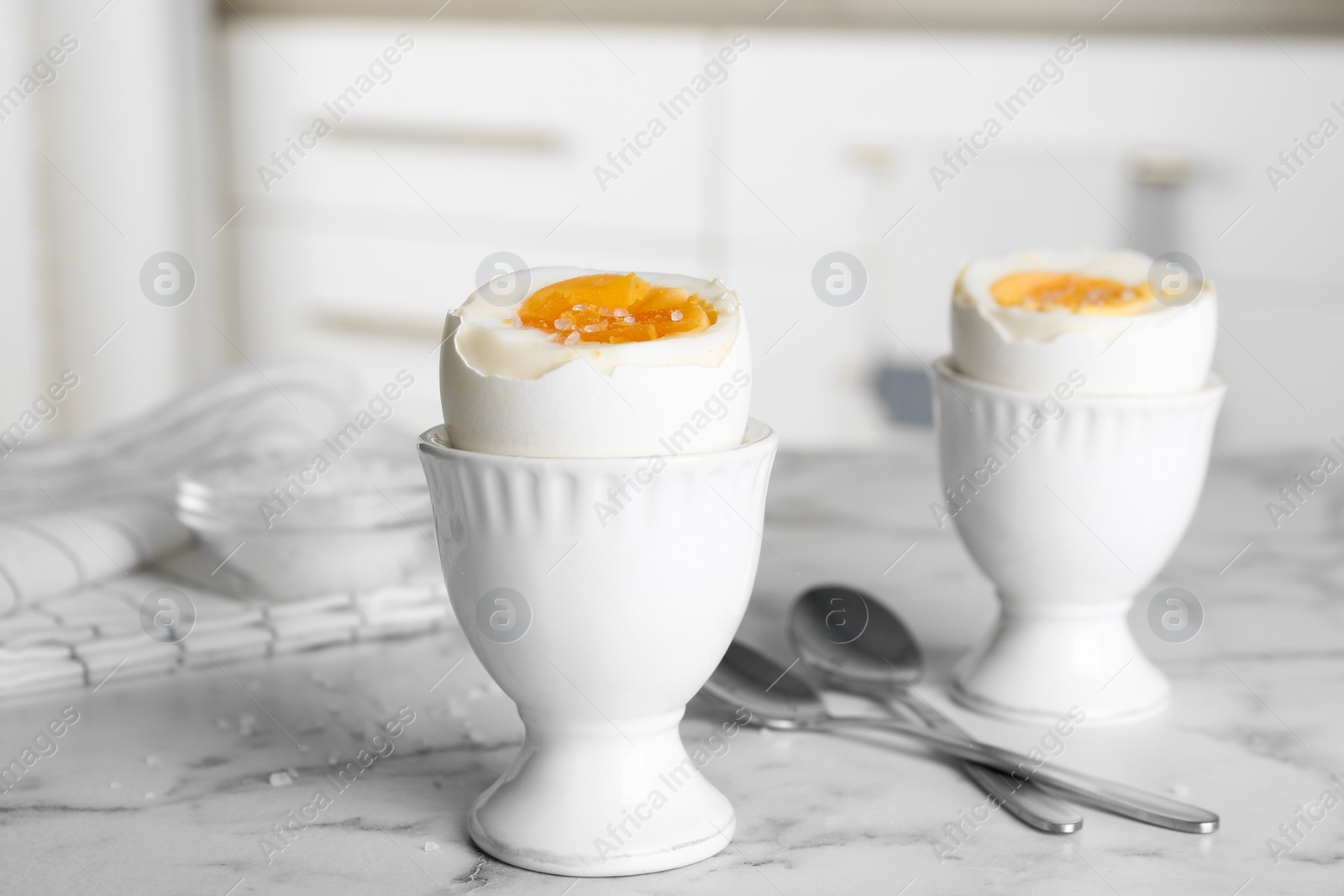 Photo of Tasty medium boiled eggs in ceramic holders on white marble table