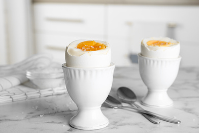 Photo of Tasty medium boiled eggs in ceramic holders on white marble table