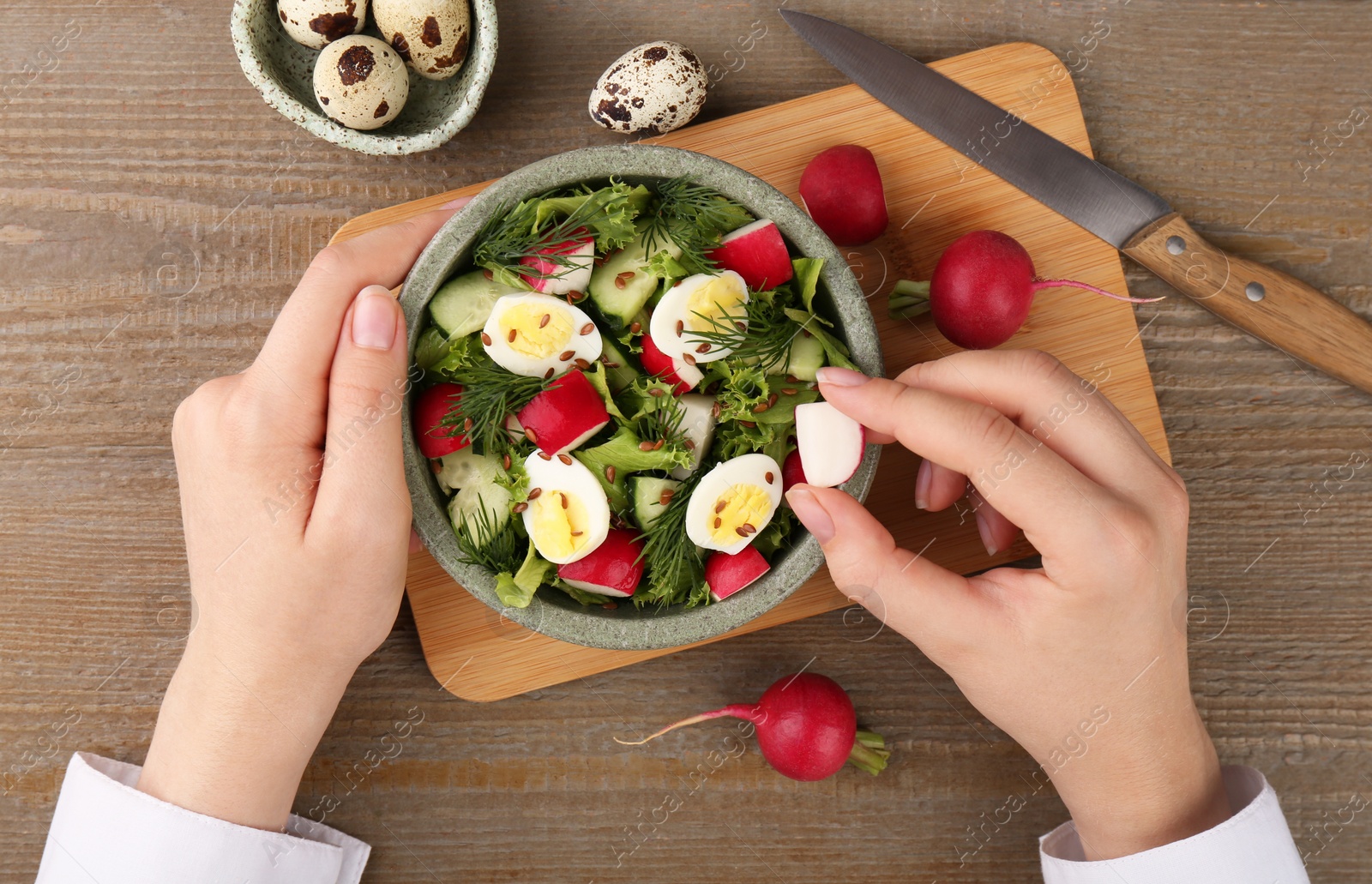 Photo of Woman adding piece of radish into salad at wooden table, top view