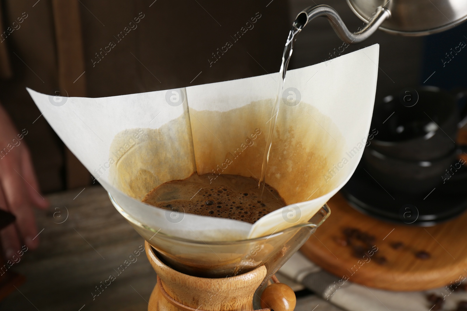 Photo of Pouring hot water into glass chemex coffeemaker with paper filter at table, closeup