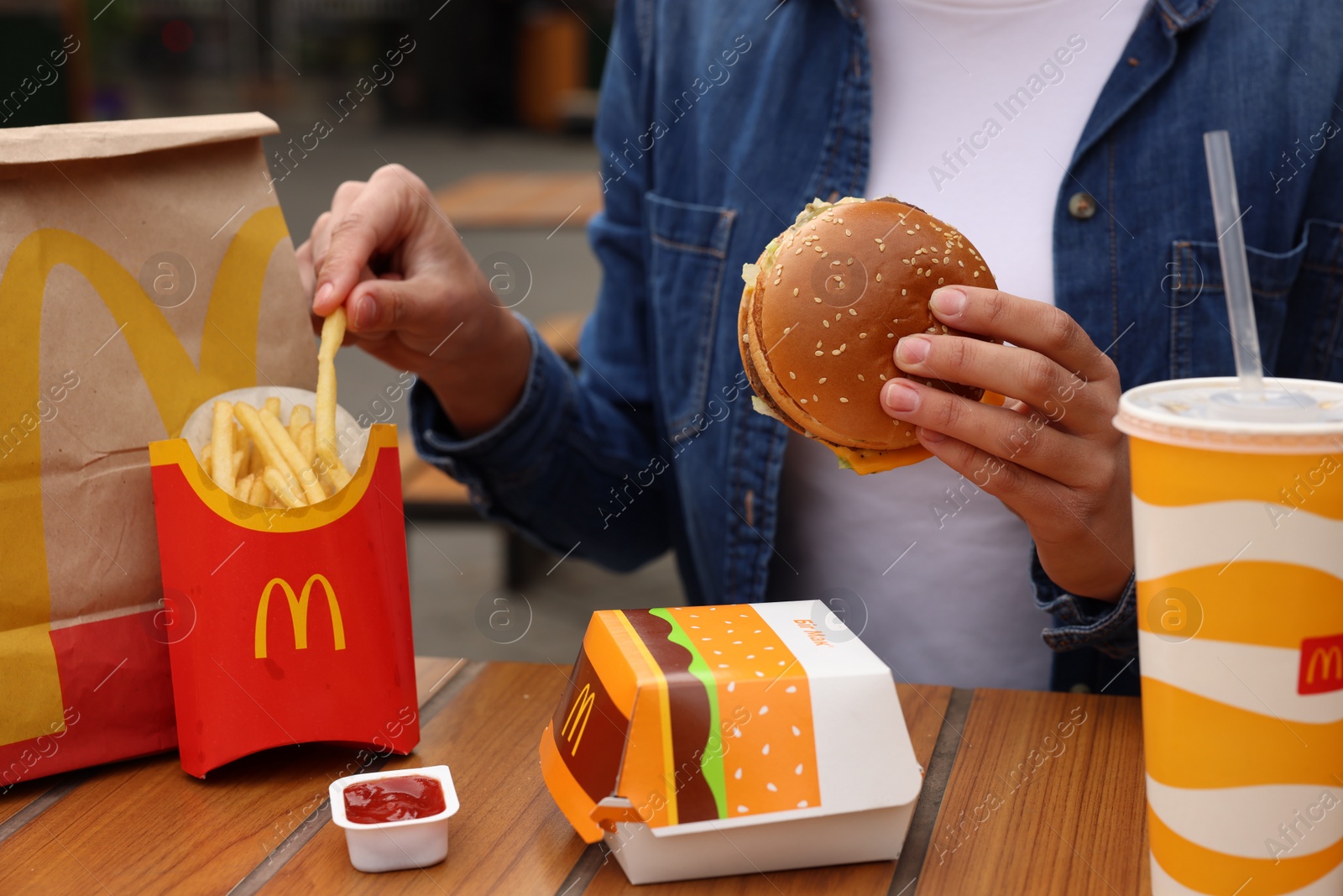 Photo of Lviv, Ukraine - October 9, 2023: Woman with McDonald's menu at wooden table outdoors, closeup