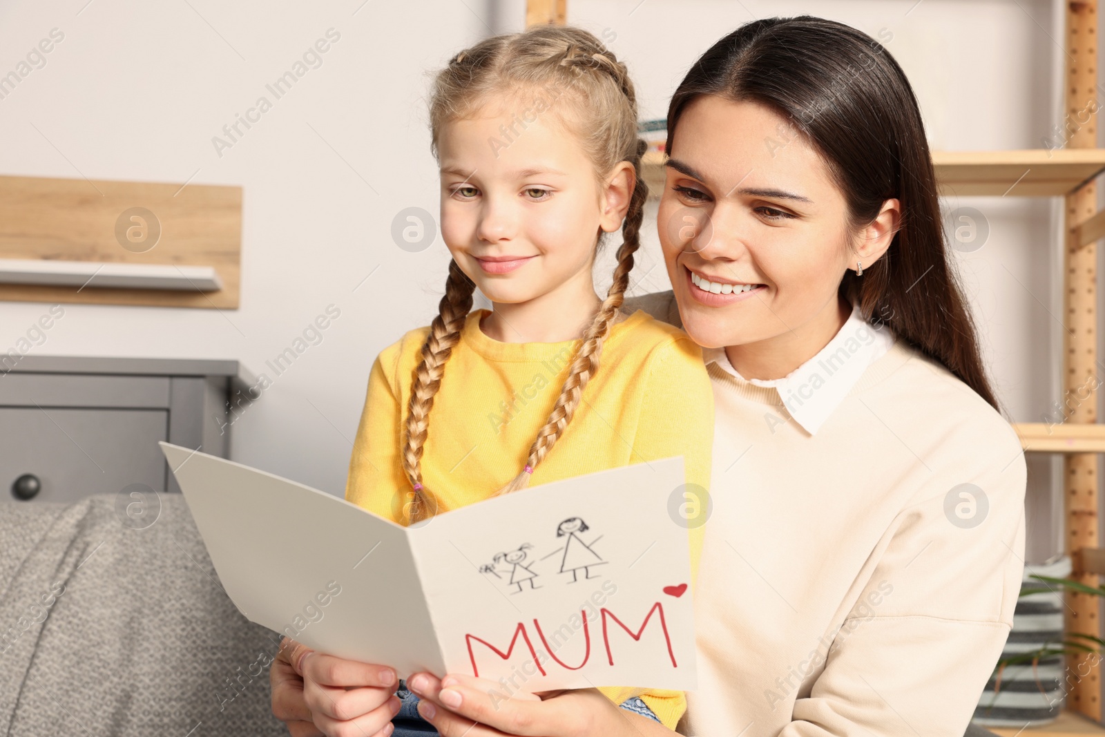 Photo of Happy woman receiving greeting card from her little daughter at home