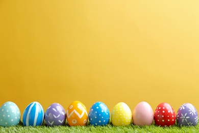 Painted Easter eggs on green grass against color background, space for text