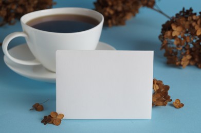 Photo of Dried hortensia flowers, sheet of paper and cup with coffee on light blue background. Space for text