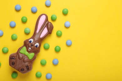 Chocolate Easter bunny and candies on yellow background, flat lay. Space for text