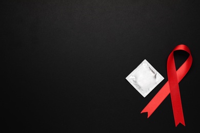 Photo of Red ribbon and condom on black background, flat lay with space for text. AIDS disease awareness