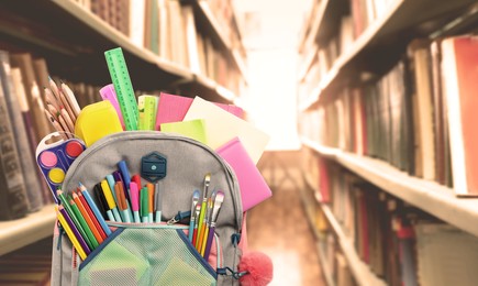 Image of Backpack with school stationery on wooden table in library, space for text