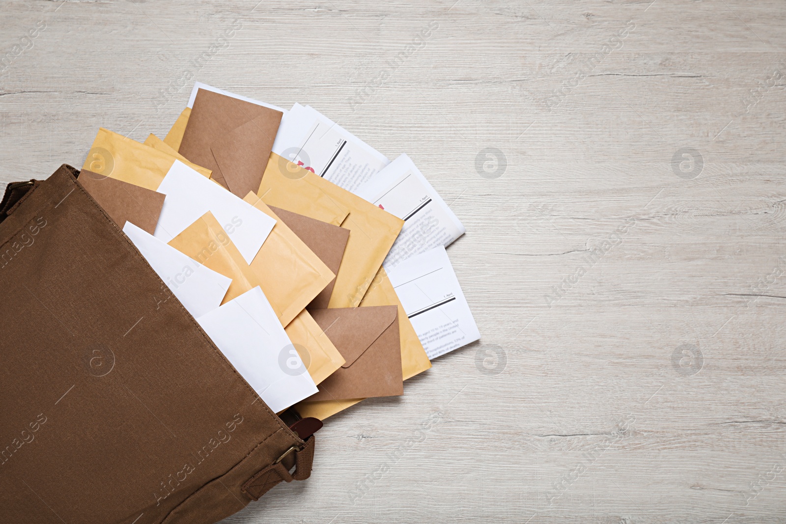 Photo of Brown postman bag with newspapers and mails on white wooden table, flat lay. Space for text