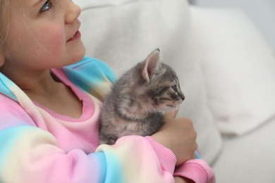 Little girl with cute fluffy kitten on sofa, closeup. Space for text