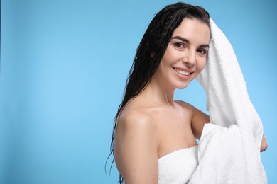 Photo of Happy young woman drying hair with towel after washing on light blue background. Space for text